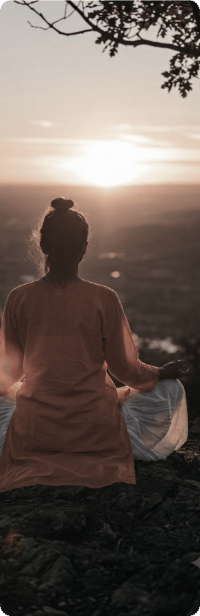 A woman sitting in stillness, facing the sunrise over the hills